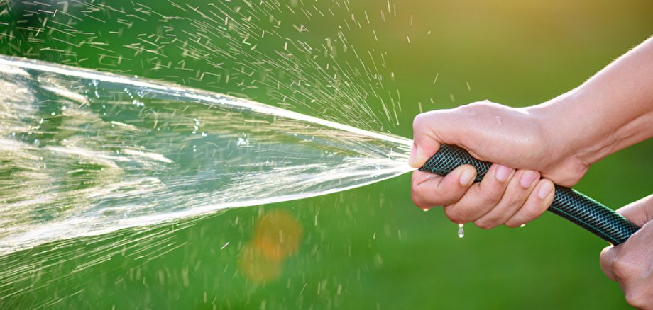 Nahaufnahme von zwei Händen, die einen Gartenschlauch halten aus dem Wasser herausspritzt