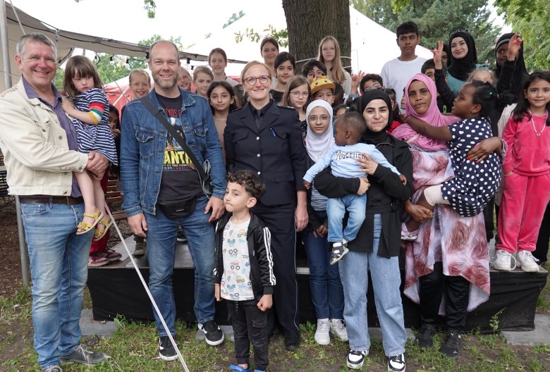 Eine größere Gruppe mit vier Erwachsenen im Vordergrund und zahlreichen Kindern stehen zusammen und lächeln in die Kamera.