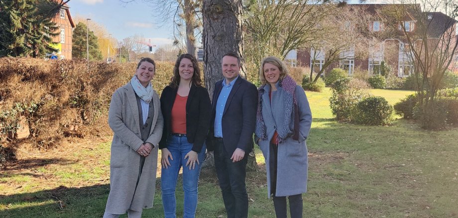 Vier Personen stehen vor einem Baum auf einer Wiese. Alle vier Lächeln freundlich in die Kamera.