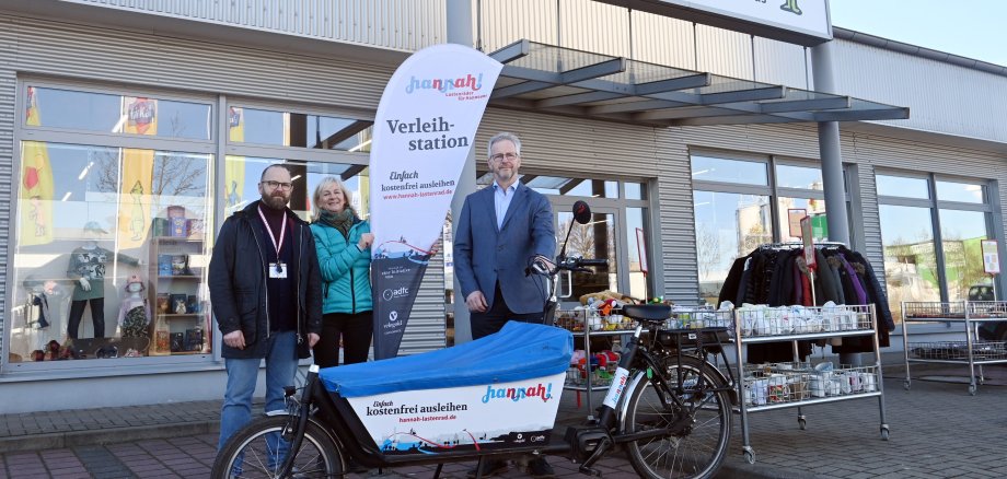 drei Personen stehen vor der fairKauf-Filia in Neustadt. davor steht das Lastenrad Hannah. Alle lächeln in die Kamera