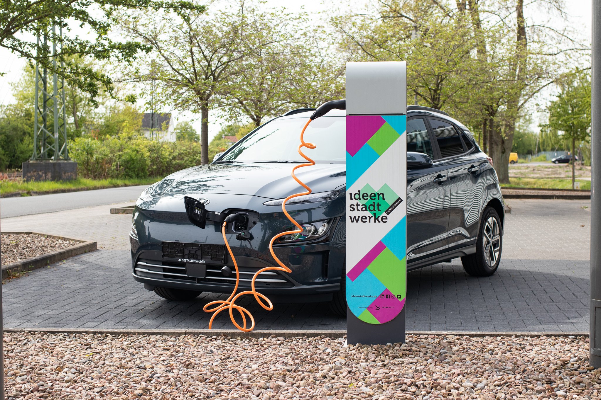 Ein schwarzes E-Auto steht auf einem Parkplatz und ist an eine E-Ladesäule der Ideenstadtwerke angeschlossen. 