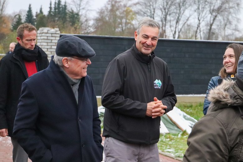 Mehrere Personen gehen draußen durch das Wohnquartier, Herr Weil udn Herr Lindauer sind im Gespräch.