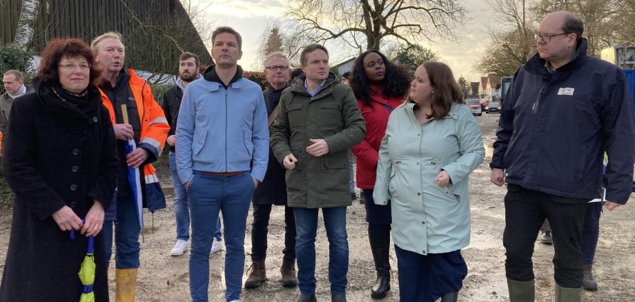 Mehre Personen stehen im Halbkreis an der Deichbaustelle im Silbernkamp.