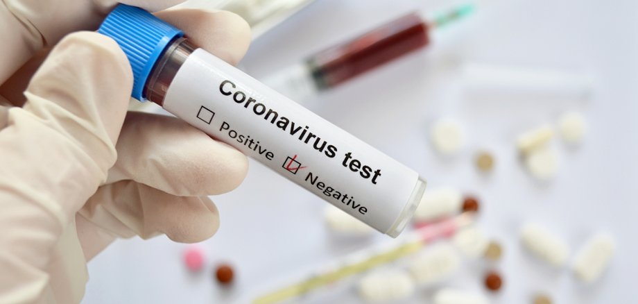 Symbolbild Corona-Test negativ Reagenzglas mit Blutprobe und negativem Testergebnis für eine Coronavirus-Infektion in der Hand eines Arztes in Gummihandschuhen auf weißem, defokussiertem Hintergrund mit Medikamenten, Nahaufnahme