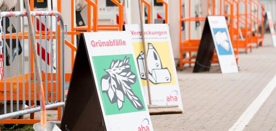 Aufnahme von Containern auf einem Wertstoffhof der aha. Im Vordergrund stehen Schilder zu den Inhalten der Container.