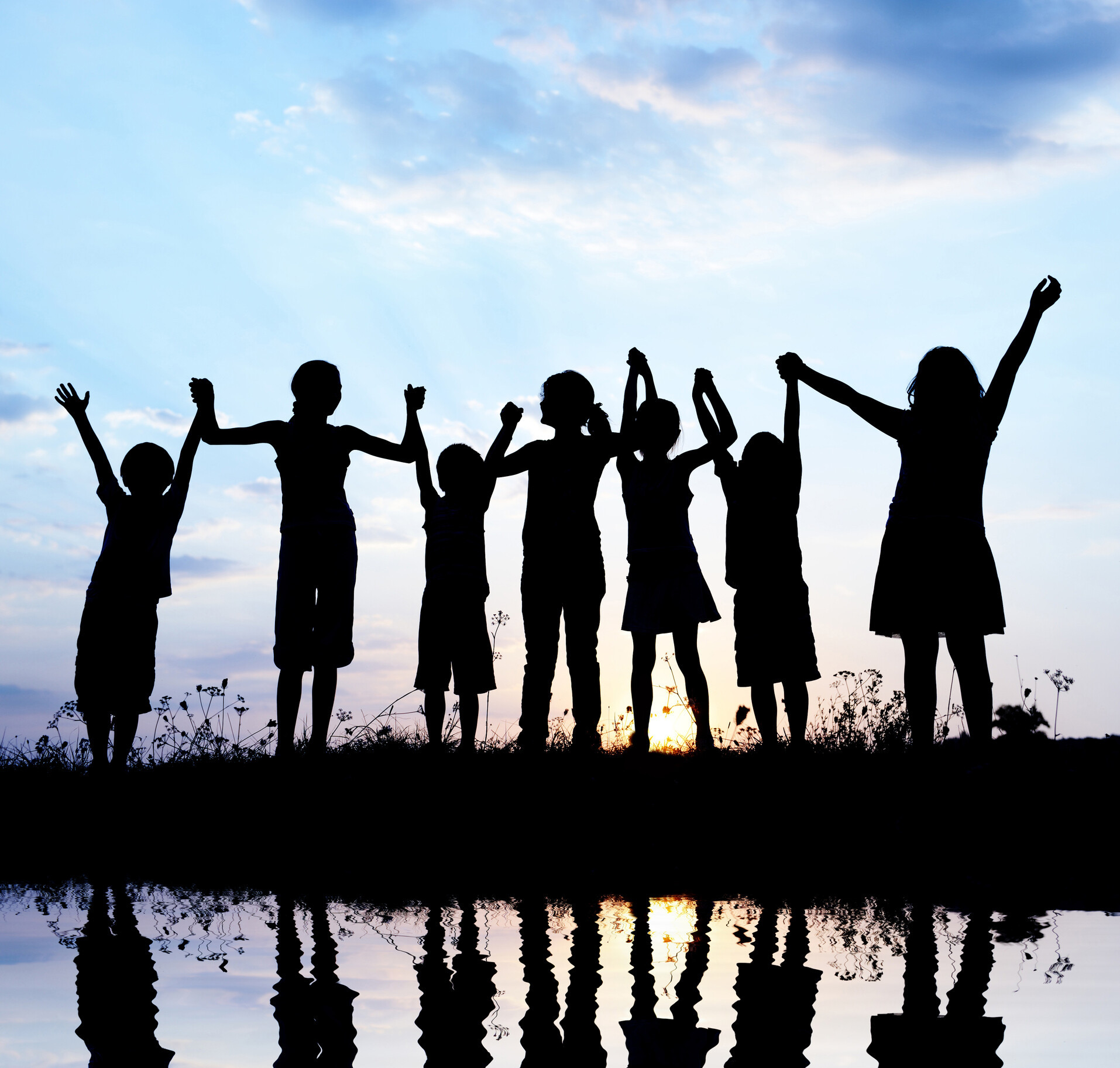 zu sehen ist eine Reihe Personen, die unterschiedlich groß sind und sich im Sonnenuntergang von den Händen halten