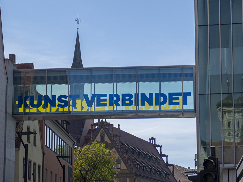 es wird eine Glasbrücke mit der Aufschrift "Kunst verbindet" gezeigt