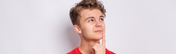 Symbolbild Frage/Umfrage Jugend Ein Jugendlicher im roten T-Shirt schaut nachdenklich nach oben rechts. Er steht vor hellem Hintergrund.