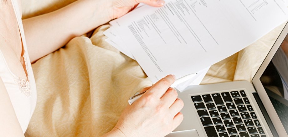 Symbolbild Homeoffice/Homeschooling Nahaufnahme von einer jungen Person, die mit einem Laptop auf den Schoss arbeitet.
