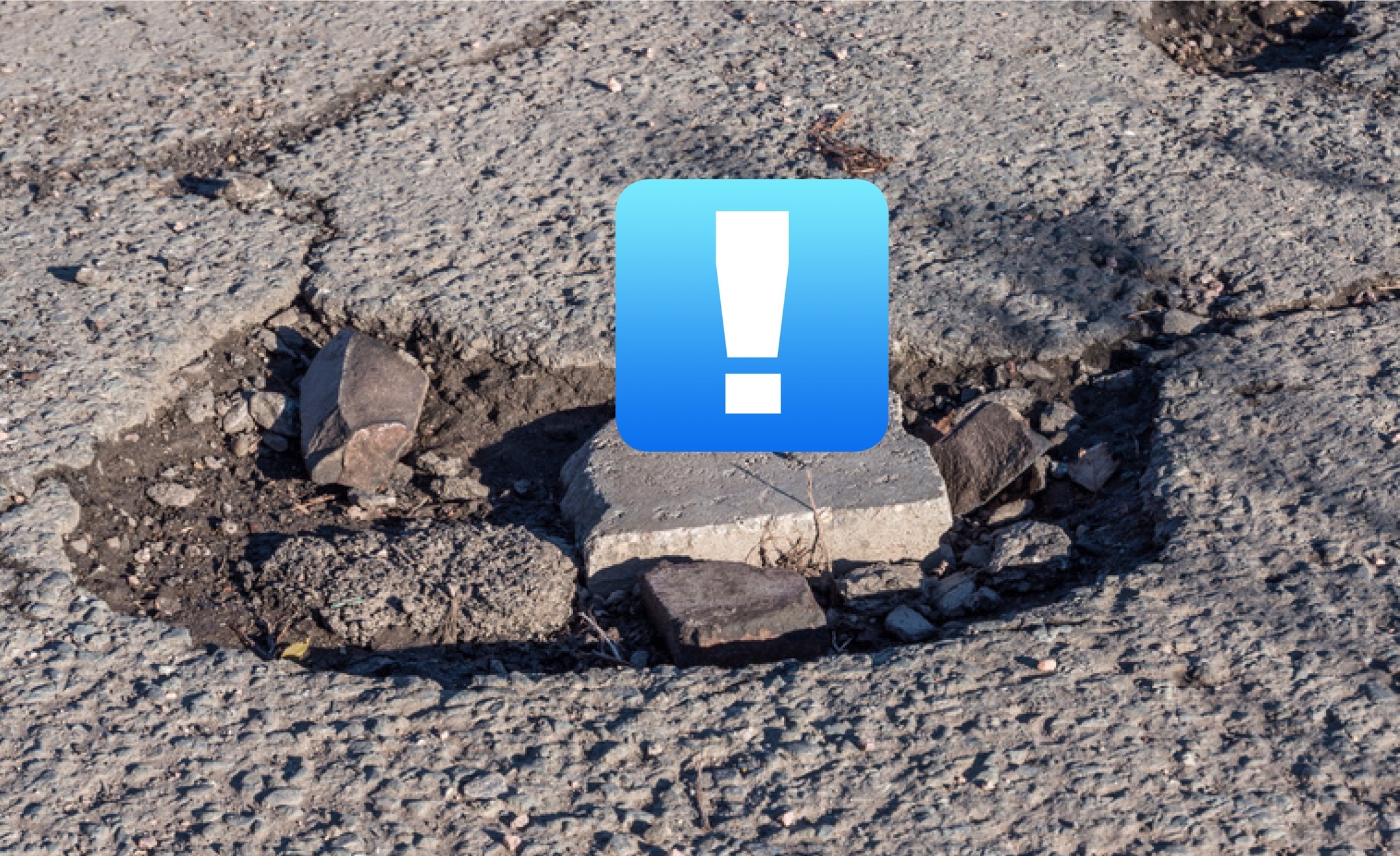 zu sehen ist eine Nahaufnahme eines Schlagloches, darauf prangt ein "!" in einem blauen Kasten