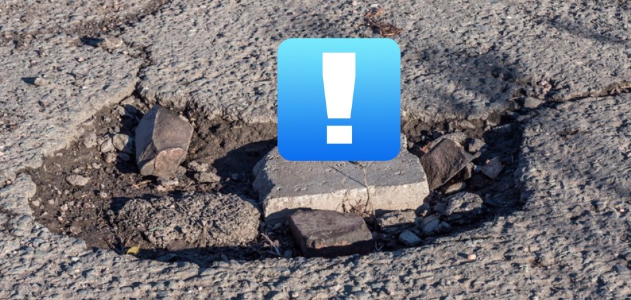 zu sehen ist eine Nahaufnahme eines Schlagloches, darauf prangt ein "!" in einem blauen Kasten