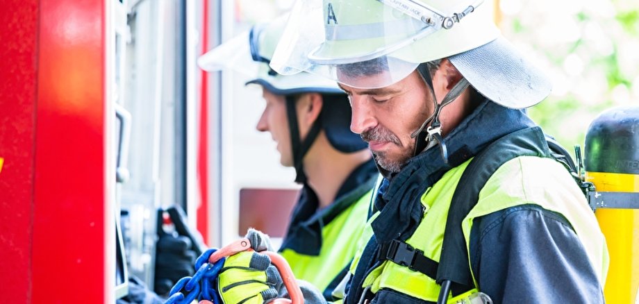 Symbolbild Feuerwehr Feuerwehrmann überprüft Schläuche am Feuerwehrauto