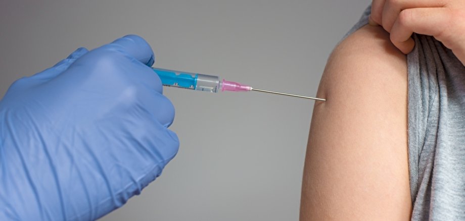 Nahaufnahme einer Impfsituation. Eine Hand im Latexhandschuh setzt eine Spritze in einen Oberarm.
