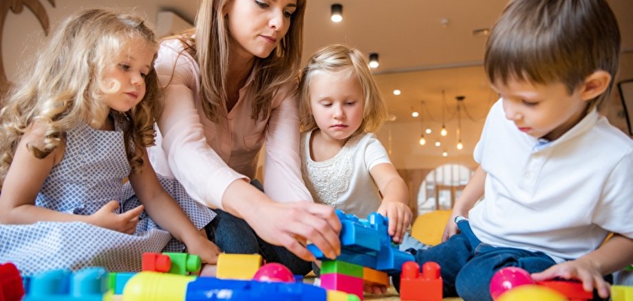 Erzieherin und liebenswerte Kinder spielen mit Bauklötzen im Kindergarten