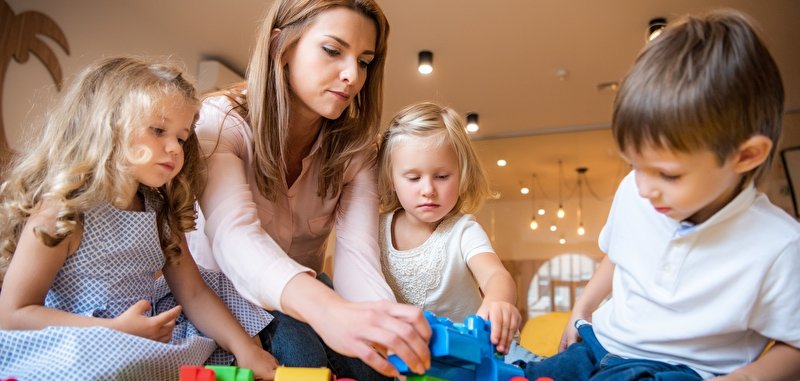 Erzieherin und liebenswerte Kinder spielen mit Bauklötzen im Kindergarten