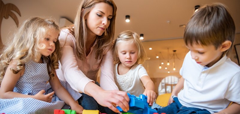 Erzieherin und liebenswerte Kinder spielen mit Bauklötzen im Kindergarten