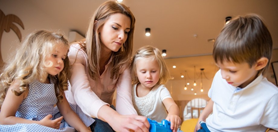 Symbolbild Kita Erzieherin und Kinder spielen mit Bauklötzen im Kindergarten