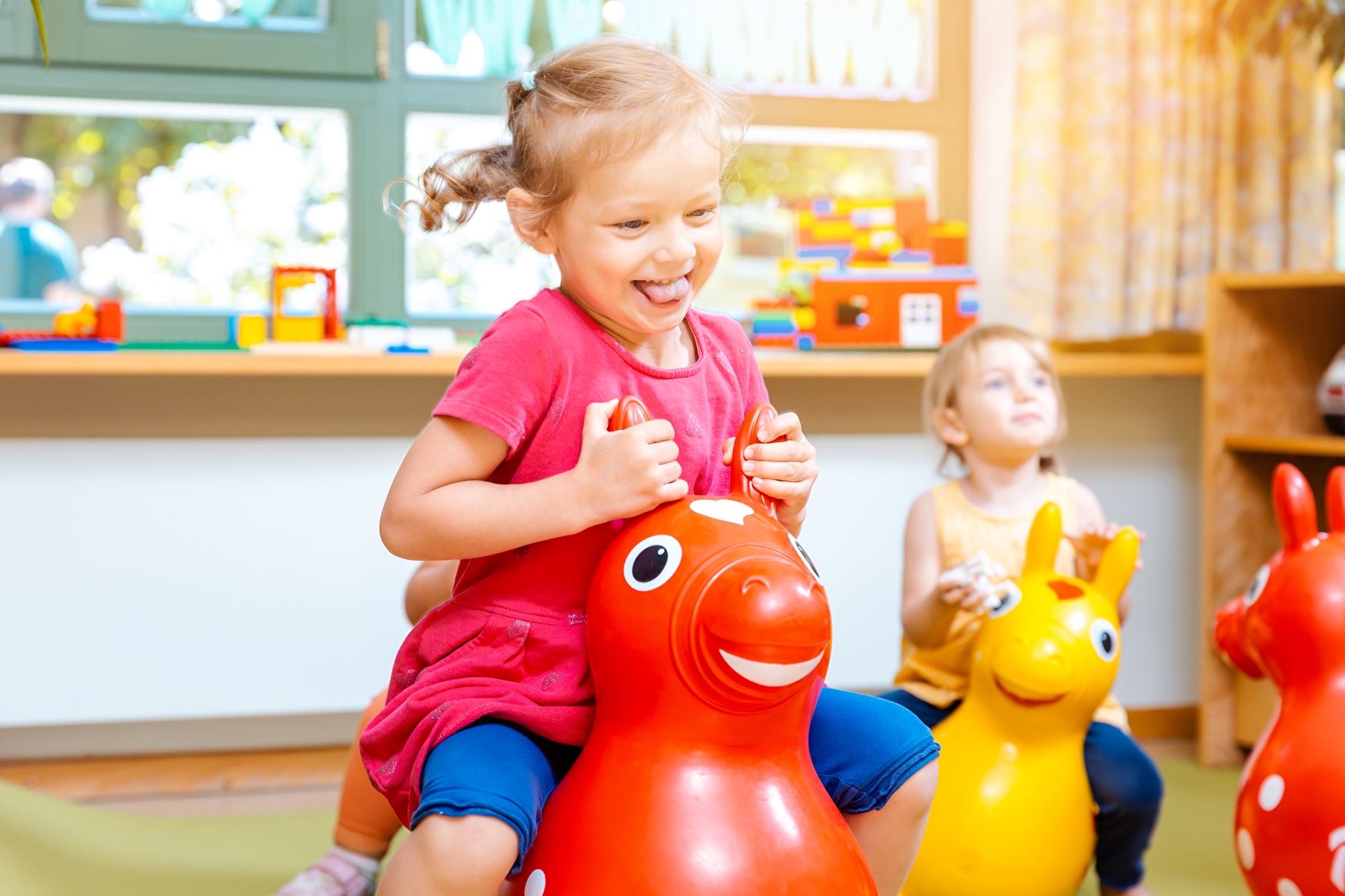 Kleine Mädchen reiten auf Spielpferden im Kindergarten