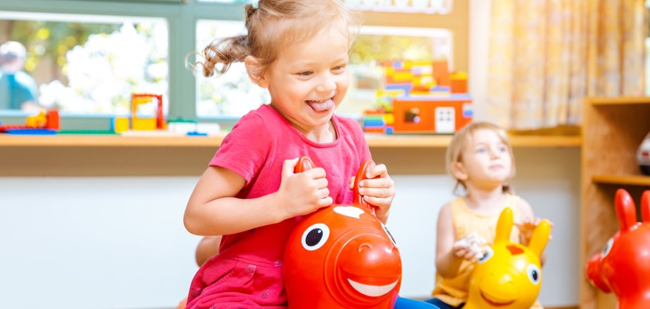 Symbolbild Kindergarten Kita Kleine Mädchen reiten auf Spielpferden im Kindergarten