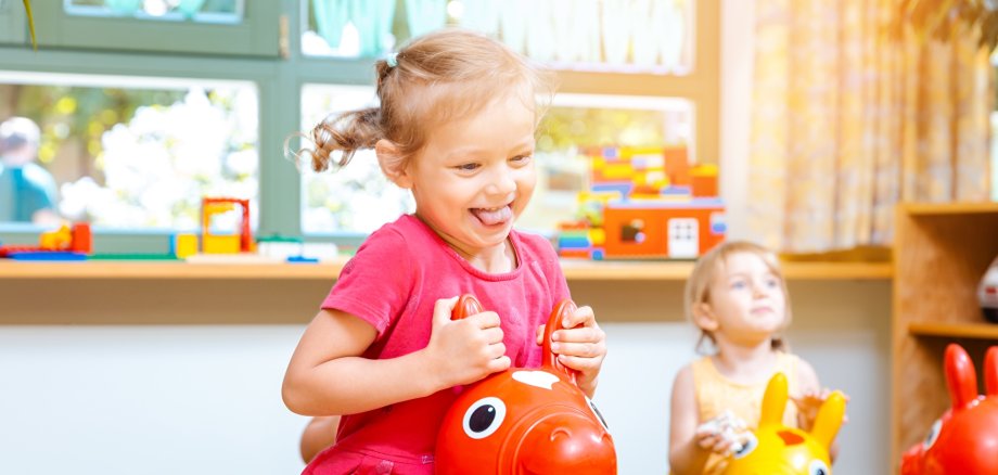 Symbolbild Kindergarten Kita Kleine Mädchen reiten auf Spielpferden im Kindergarten