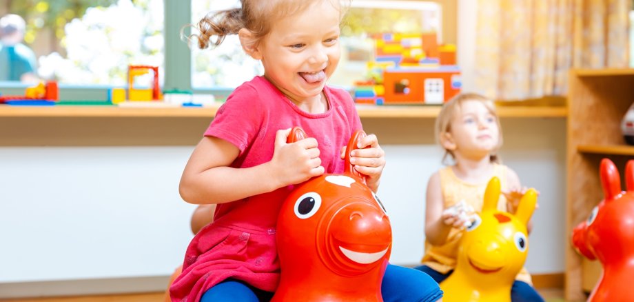 Kleine Mädchen reiten auf Spielpferden im Kindergarten