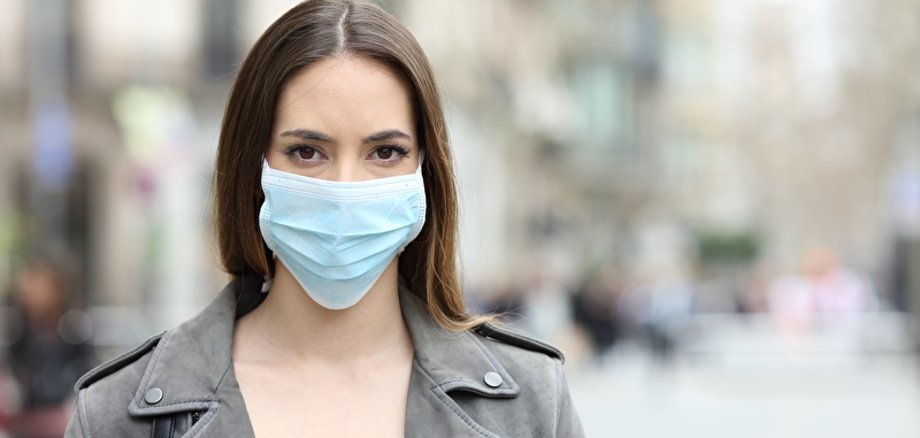 Eine junge Frau steht draußen und trägt eine OP-Maske.