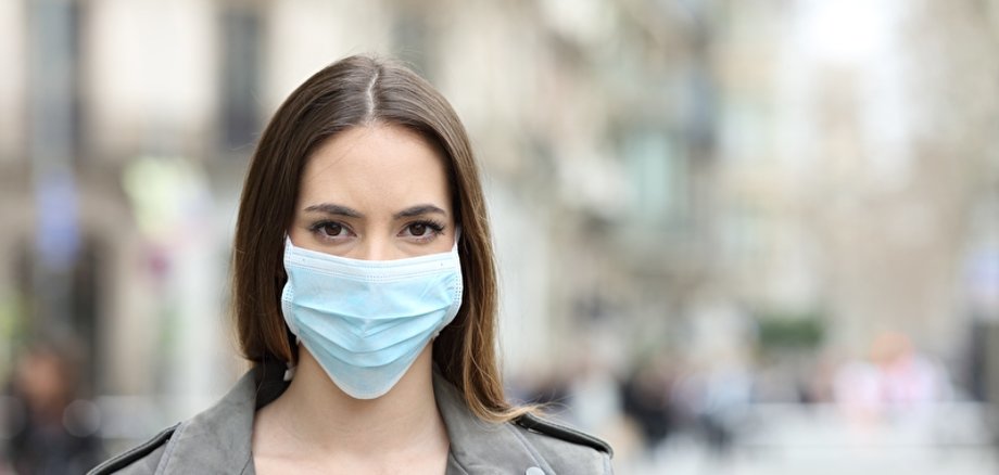 Symbolbild Maske Eine junge Frau steht draußen und trägt eine OP-Maske.
