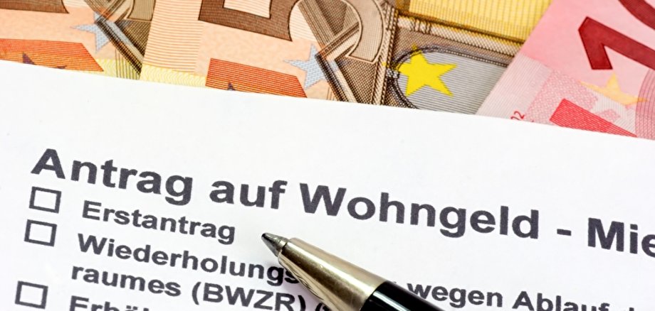 Wohngeld zu sehen sind ein Antrag auf Wohngeld und ein Stift, im Hintergrund liegen Geldscheine