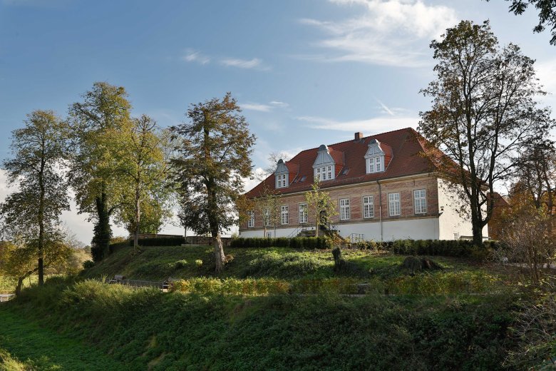 Blick auf das Schloss landestrost. Das Schlossgebäude steht auf einem grünen Hügel, umrandet von Bäumen.