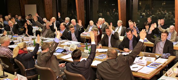 Rat der Stadt Neustadt a. Rbge. Szene aus einer Ratssitzung. Die Ratsmitglieder stimmen per Handzeichen über eine Vorlage ab.