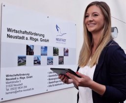 Blick nach vorn Eine Frau mit Tablet in der Hand steht vor der WIrtschaftsförderung und wendet sich freudig entschlossen ab