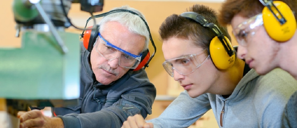 Anleitung von Auszubildenden Ein Mitarbeiter an einer Maschine zeigt zwei jungen Auszubildenden die Arbeit mit Holz