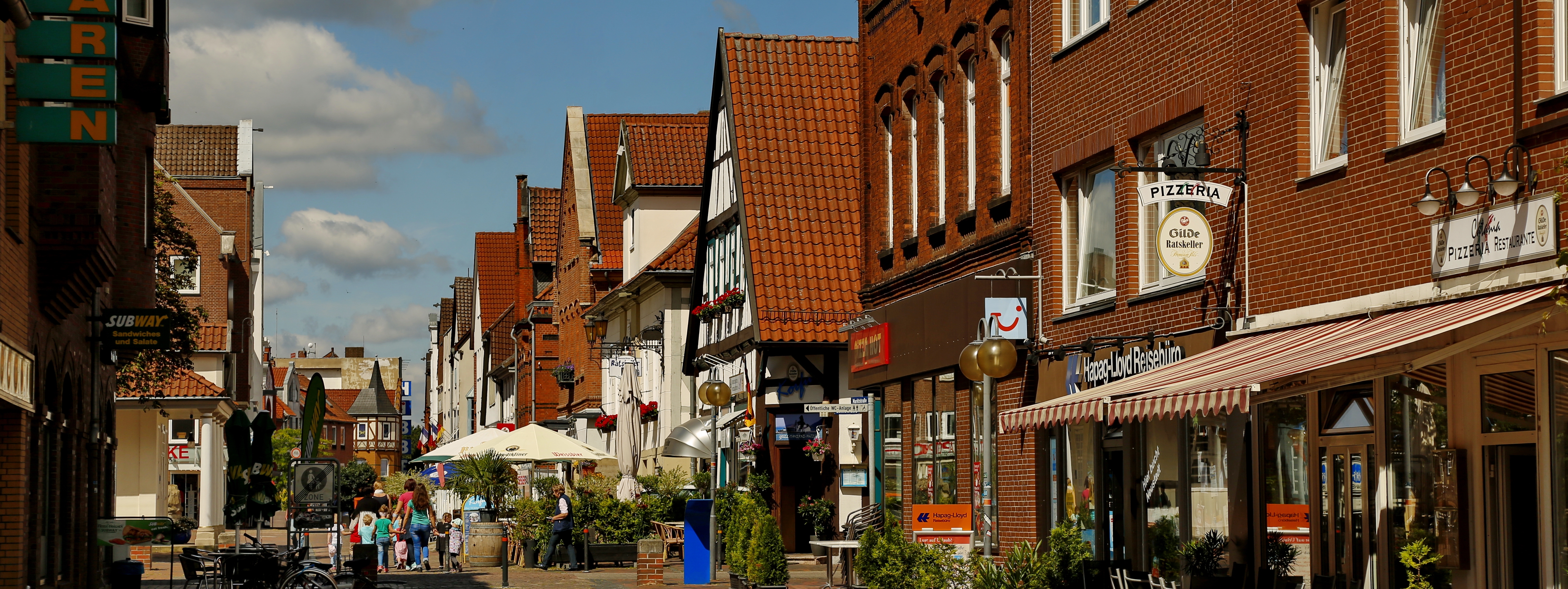 Die Marktstraße ist die Hauptgeschäftsstraße der Neustädter Innenstadt. Passanten laufen in der Fußgängerzone von Neustadt entlang der Hauptgeschäftstraße Richtung Zentrum