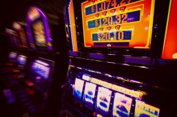 Spielautomat im Casino Im Vordergrund ein gelb/oranger Spielautomat, im Hintergrund unscharf drei weitere Spielautomaten